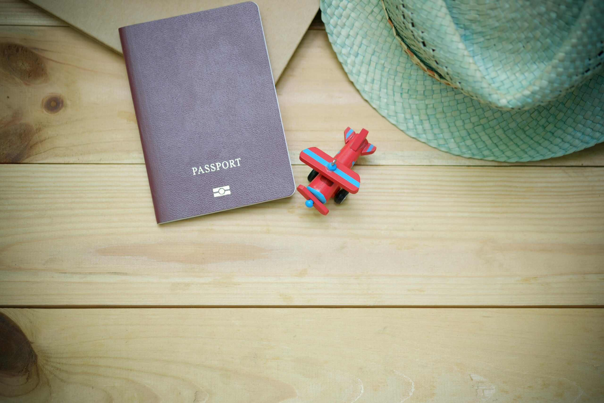 pexels-photo-346798-346798 Flat lay of a passport, straw hat, and toy airplane on a wooden surface.
